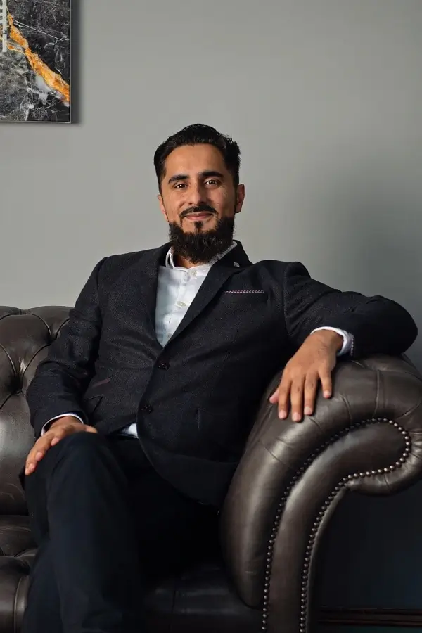 A man with a beard lounging on a leather couch, showcasing a casual and thoughtful expression.