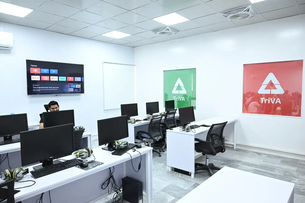 A man sits at a desk in a room filled with multiple computers, engaged in his work.