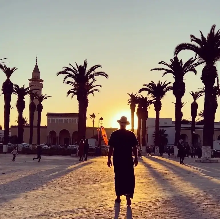 A man walks alone in a plaza during sunset, with vibrant colors illuminating the sky and creating a serene atmosphere.